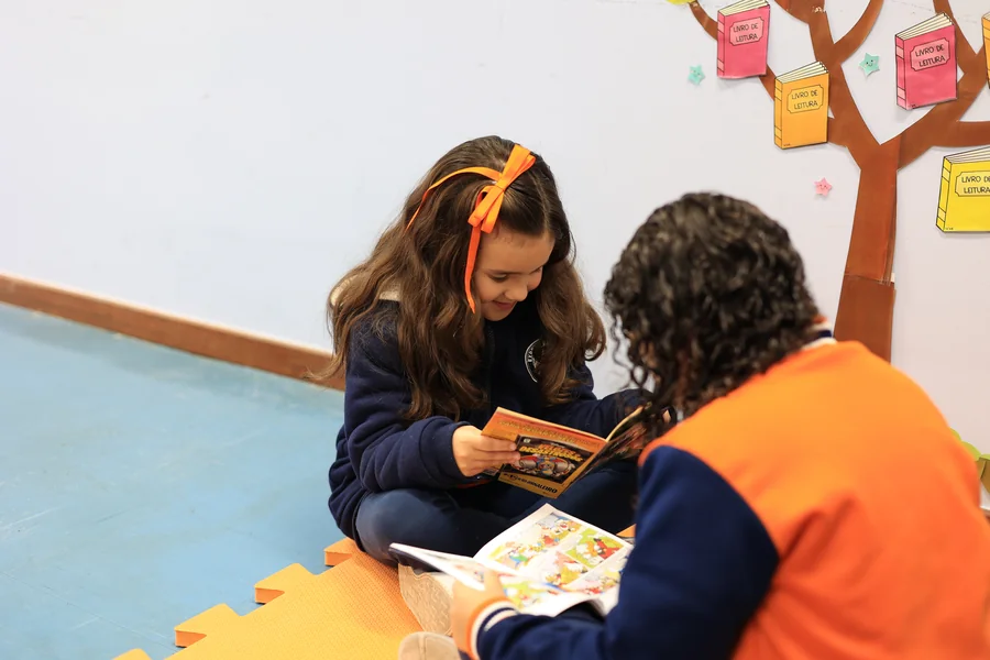 Aluna e professora lendo um livro sentadas no chão da sala