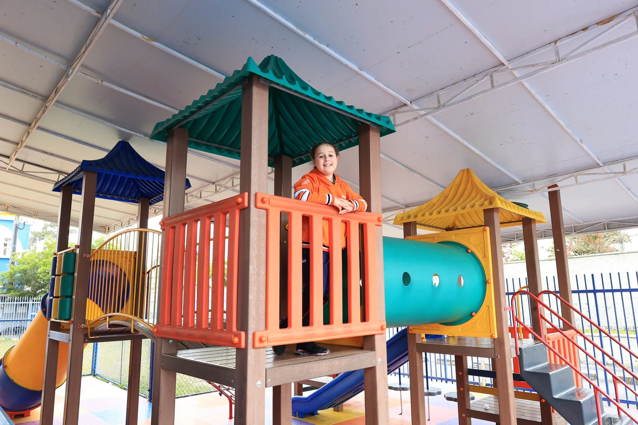 Aluna do Colégio Acesso sorrindo em cima de brinquedo do playground