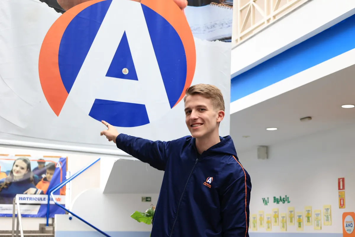 Aluno do Ensino Médio do Colégio Acesso apontando para o logo da escola