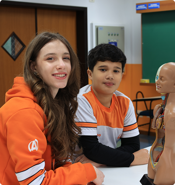 Aluna do Ensino Fundamental do Colégio Acesso apoiada em mesa com modelo anatômico em sala de aula